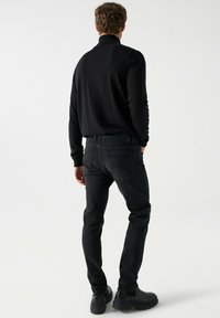 Črna majica z dolgimi rokavi, prilegajoča se zasnova, v kombinaciji z temno kavbojkami. Obleka se ponaša s sijočo teksturo in minimalističnim slogom. Črni škornji dopolnjujejo videz.