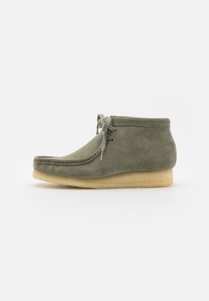 Green suede ankle boot with a rounded toe, minimal stitching, and a beige rubber sole. Features a lace-up front for secure fastening.