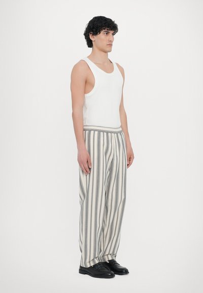 White tank top, striped pants in beige and grey, wide leg design, elastic waist, paired with black shoes. Standing pose against a white background.