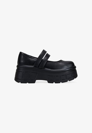 Zapato negro tipo Mary Jane con suela gruesa y dos correas en la parte superior, visto de lado sobre un fondo blanco.