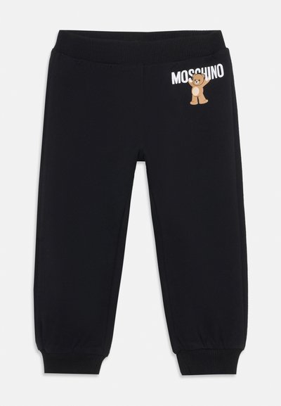 Čierne tepláky s ribovaným pásom a manžetami. Na ľavom stehne sa nachádza biele logo "Moschino" a grafika hnedého medveďa.