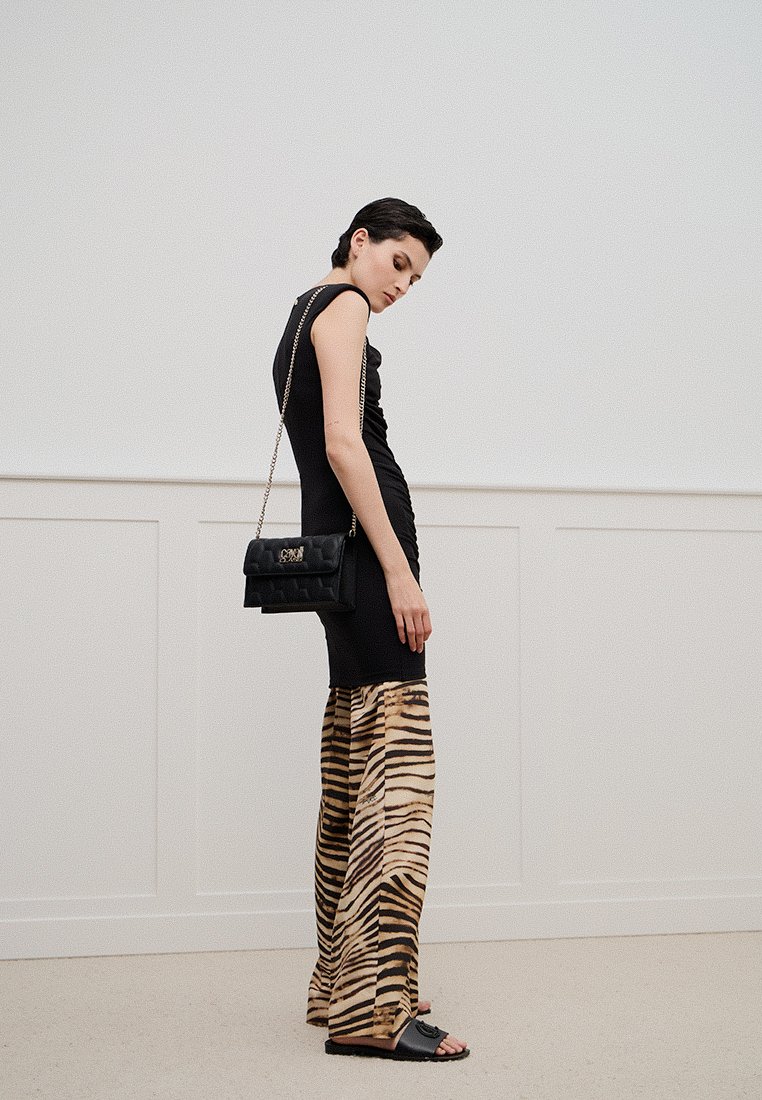 Mujer vistiendo una blusa negra sin mangas, pantalones de pierna ancha con estampado de tigre, sandalias negras y llevando un bolso negro acolchado con cadena.