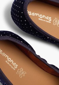 Tmavě modré baletní byty s texturovaným povrchem, zdobené bílými puntíky a hnědou koženou stélkou s raženými detaily značky.