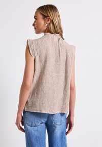 Top senza maniche a righe in beige e marrone, con un colletto alto e una vestibilità comoda. Abbinato a jeans di denim blu chiaro.
