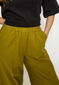 Laiade püksid pehmest oliivrohelisest kangast, millel on elastne vöökoht ja küljetaskud, sobitatud musta topiga.