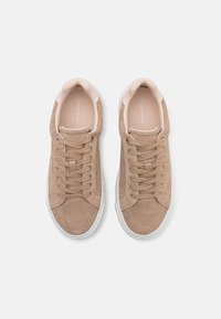 Hellbraune Wildledersneaker mit einer weißen Gummisohle, runden Schnürsenkeln und einem gepolsterten Schaft. Der Markenname "Calvin Klein" ist innen aufgedruckt.