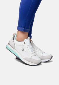 Vita och grå sportskor med perforerade sektioner, silverdetaljer och en turkos sula. Har snörning och varumärkeslogga på sidan.