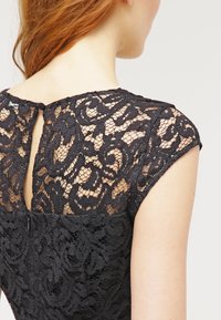 Svart spetsklänning med mönstrad genomskinlig bakdel, korta ärmar och rund halsringning med knäppning bak.