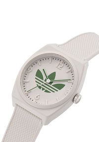 Bijela silikonska sat s kvadratnim kućištem, zeleni cvjetni logo na bijelom brojčaniku i teksturirani bijeli remen. Srebrna krunica na boku.