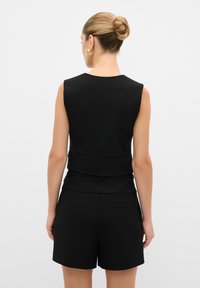 Svart ärmlös topp med en strukturerad design och en lätt peplum i midjan, matchad med svarta shorts med en detalj av bakficka.