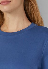 T-shirt bleu à col rond fabriqué en tissu doux, présentant une texture lisse et une couture minimale autour du col, mettant l'accent sur un design simple.