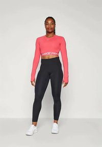 Rød langermet crop topp med "NIKE PRO" tekst, sammen med svarte høyhåndte tights og hvite treningssko på en nøytral bakgrunn.