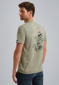 Olivegrünes Baumwoll-T-Shirt mit kurzen Ärmeln. Verfügt über ein pinkes Grafikdesign mit der Aufschrift "PME Legend" und Blattmuster auf der Rückseite.
