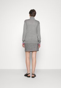 Grauer Rollkragenpullover mit strukturiertem Muster auf dem Rücken, kombiniert mit einem Tweedrock. Akzente bilden leuchtend pinkfarbene Bündchen und schwarze Sandalen.