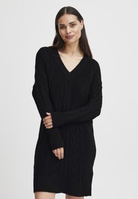 Abito maglione nero lavorato a maglia caratterizzato da scollatura a V, trama in treccia e polsini e orlo a costine. Maniche lunghe con aperture per il pollice.