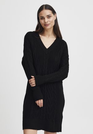 Black knitted sweater dress featuring a V-neck, cable knit texture, and ribbed cuffs and hem. Long sleeves with thumbholes.