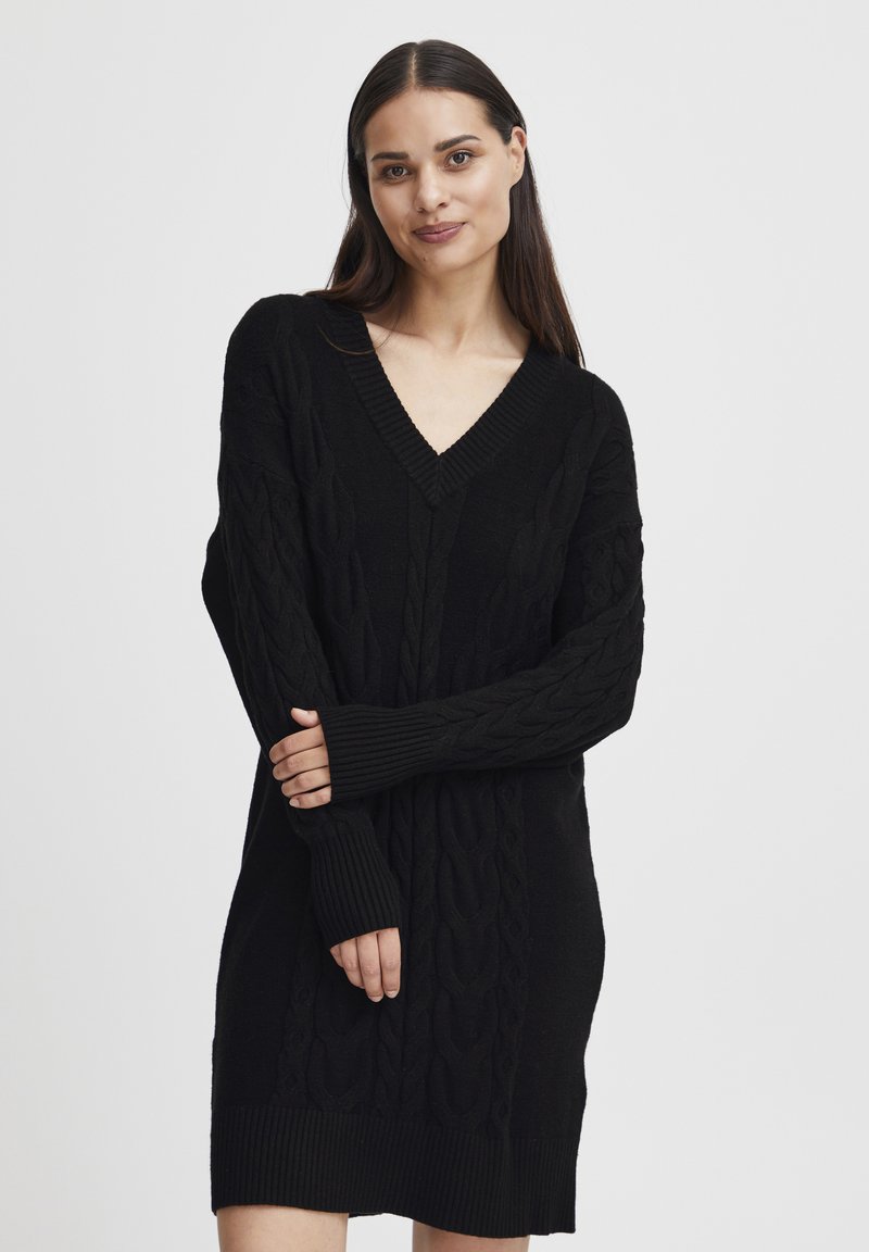 Abito maglione nero lavorato a maglia caratterizzato da scollatura a V, trama in treccia e polsini e orlo a costine. Maniche lunghe con aperture per il pollice.