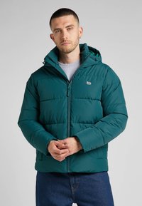 Turkusowa kurtka puchowa z kapturem, wyposażona w zamek błyskawiczny z przodu, elastyczne mankiety i naszywkę z logo na klatce piersiowej. Gładka, wyściełana tekstura.