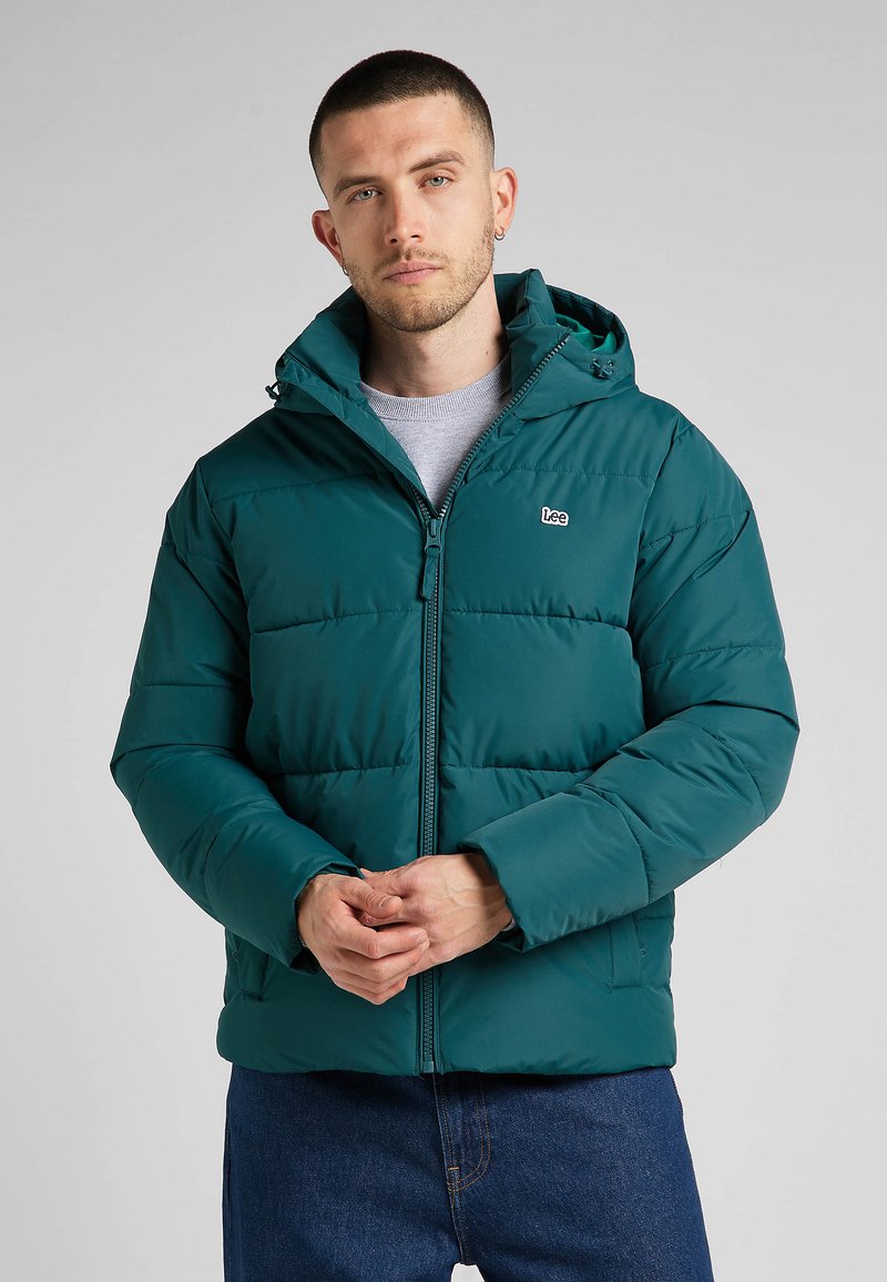 Turkusowa kurtka puchowa z kapturem, wyposażona w zamek błyskawiczny z przodu, elastyczne mankiety i naszywkę z logo na klatce piersiowej. Gładka, wyściełana tekstura.