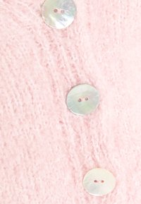 Tissu tricot doux rose avec trois grands boutons ronds blancs brillants disposés verticalement dessus.