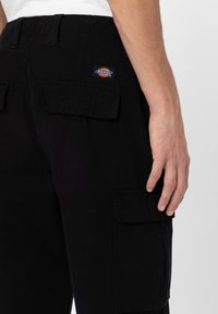 Czarne spodnie cargo z wieloma bocznymi kieszeniami, detalem z plecionym logo oraz teksturowanym materiałem. Pas wyposażony jest w szlufki na pasek.