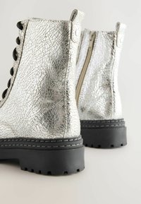 Bottines à effet craquelé argenté avec des lacets noirs, une tige texturée et une semelle en caoutchouc robuste ; dotées d'une fermeture éclair sur le côté pour un accès facile.
