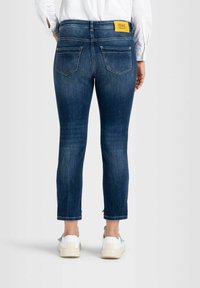 Jean court bleu foncé en denim, avec des poches arrière, une étiquette de marque jaune à la ceinture et un détail d'ourlet effiloché.