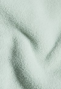 Soft, textured fabric in pale mint green, showcasing a plush, fleece-like surface with subtle light and shadow variations.