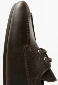 Brun lædersko med rundet tå, sydd detaljer og metaløjer til snørebånd. Overfladen fremstår glat og poleret.