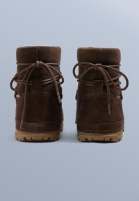 Barna velúr bokacsizma bélelt szegéllyel, fűzős kialakítással és gumitalpakkal. Díszítő varrások és kis fülök a hátsó részen.