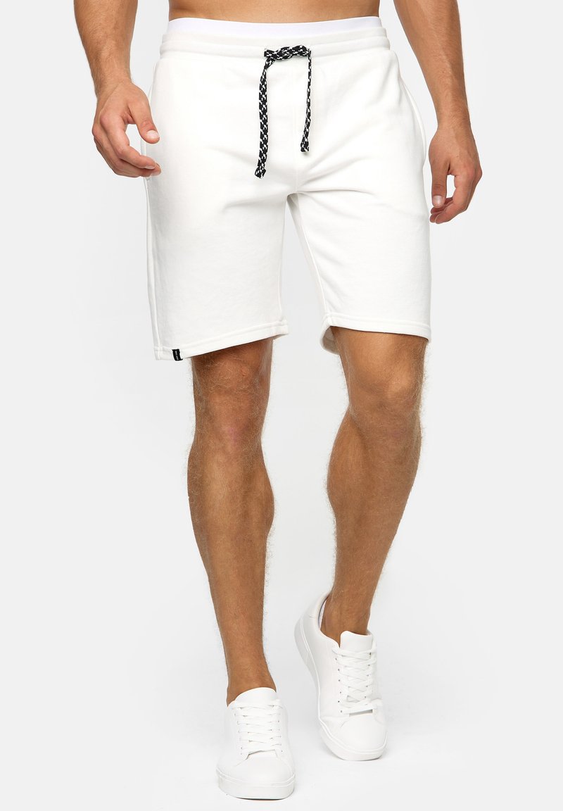 Weiße Baumwollmischung-Shorts mit einem Zugband in der Taille, ausgestattet mit einem schwarz-weißen geflochtenen Kordelzug und einem gesteppten Saum. Kombiniert mit weißen Sneakers.