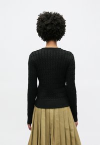 Pull en maille côtelée noire avec ourlet et poignets côtelés, associé à une jupe plissée vert olive. Tissu texturé, silhouette ajustée.