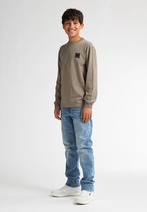 Olijfgroen shirt met lange mouwen en een zwart vierkant logo, gecombineerd met lichtblauwe denim jeans en witte sneakers. Eenvoudig ontwerp, casual pasvorm.