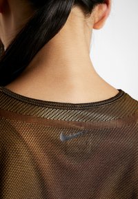 Camiseta marrón de malla de Nike con cuello redondo y un logo sutil en la parte posterior. La textura del tejido es ligera y transpirable.