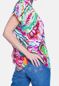 Lyhythihainen kukkakuosiset paita kirkkaissa väreissä, jossa on kevyt kangas ja kaareva helma, yhdistettynä vaaleisiin farkkuihin.