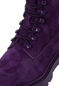 Stivale viola in suede con superficie testurizzata, dotato di lacci e occhielli viola scuro. La suola intermedia presenta un design solido e a contrasto.