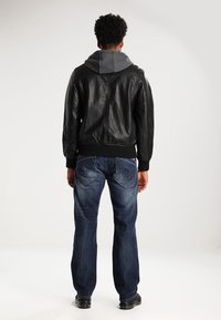 Svart läderjacka med en grå huvtröja under, parat med blå denimjeans. Jeansen har bakfickor med ett distinkt sömmönster.