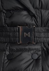 Černá péřovka s texturovanou tkaninou, velkými černými knoflíky a staženým elastickým páskem s kovovou sponou vyrytou písmenem "M."