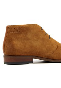 Tan suede ankle boot with a smooth brown leather heel, blue laces, and subtle stitching details. Features a low stacked heel.