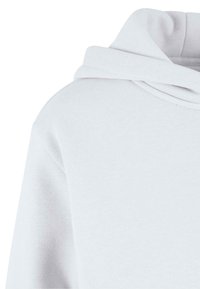 Sweat à capuche blanc avec un tissu doux et texturé, une grande capuche et un large décolleté, avec des coutures visibles le long des coutures.