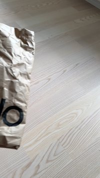 Busta di carta marrone stropicciata con un grande grafico circolare nero, appoggiata su un pavimento in legno chiaro con evidenti venature.