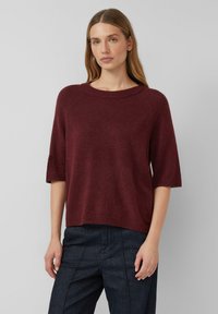 Pull en tricot bordeaux avec un large décolleté rond, des manches raglan courtes, et une coupe ample, avec une finition douce et texturée.