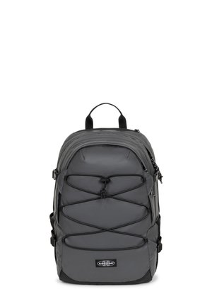 Mochila gris con un tejido resistente, que presenta un diseño de cordón elástico en la parte frontal, un asa superior y correas ajustables para mayor comodidad y utilidad.