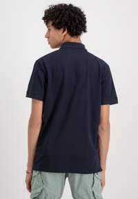 Polo shirt navy con maniche corte, colletto e texture liscia. Presenta un logo sottile sulla manica e una vestibilità rilassata.