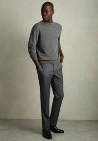 Pull en tricot gris avec motif en losanges, associé à un pantalon gris ajusté. Des chaussures noires complètent l'ensemble. Fond neutre.