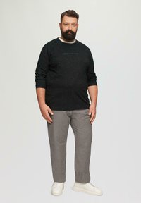 Schwarzes Sweatshirt mit strukturierten Sprenkeln, Rundhalsausschnitt und langen Ärmeln, kombiniert mit hellgrauen gemusterten Hosen und weißen Sneakers.