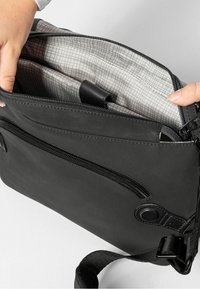 Schwarze Umhängetasche mit zwei Reißverschlussfächern, ausgestattet mit einem gittermusterartigen Innenfutter und einem abnehmbaren Tragriemen. Strapazierfähiges Material mit glatter Textur.
