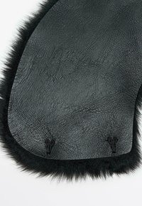 Sort kunstlædermateriale med en tekstureret overflade, omkranset af blød sort pels. Har to kroge til fastgørelse i bunden.