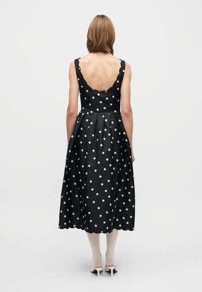 Svart klänning med prickar, klockad kjol, scalloped urringning och tunna band. Har vita prickar och en figurnära överdel.