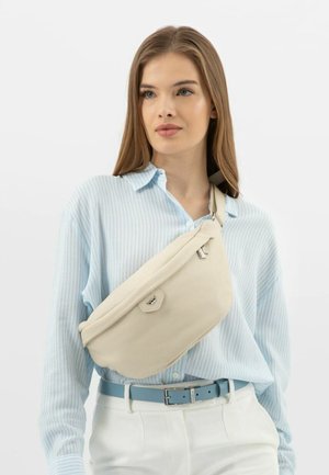 Borsa a tracolla beige realizzata in materiale texturizzato, con chiusura a zip e un sottile dettaglio in metallo, indossata sopra una camicia a righe blu chiaro.